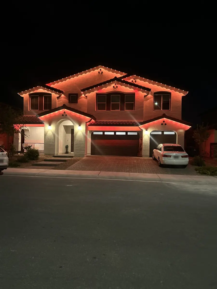Permanent eave lighting in warm orange outlining the rooflines of a two-story stucco home at night, Las Vegas